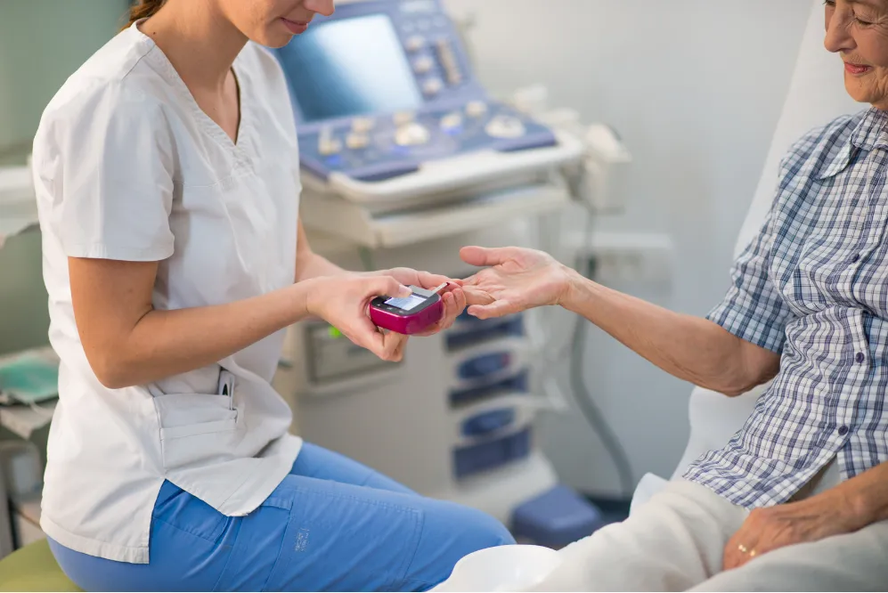 A nurse checks an older patient’s blood sugar with a glucometer in a medical clinic.