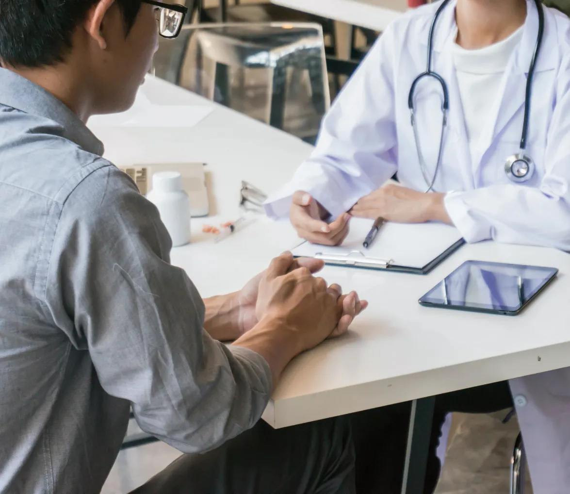 Patient talking to a doctor at a desk with a tablet, clipboard, and medicine bottle on the table.