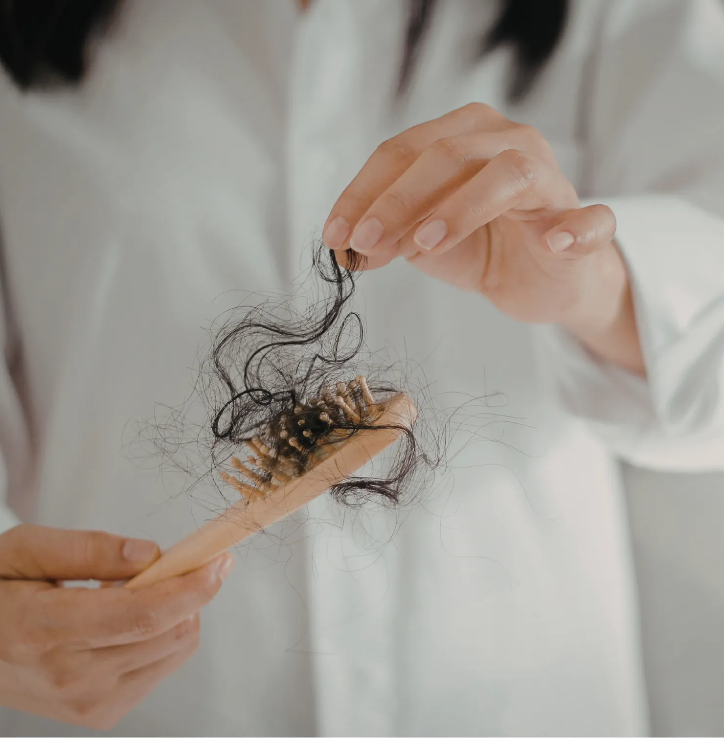 Person holding a hairbrush with clumps of dark hair tangled in the bristles and fingers.