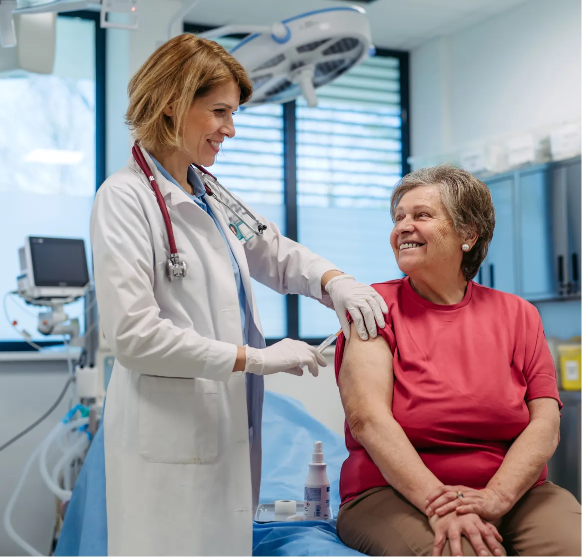 A doctor prepares to give a smiling elderly woman a vaccine in a medical clinic.