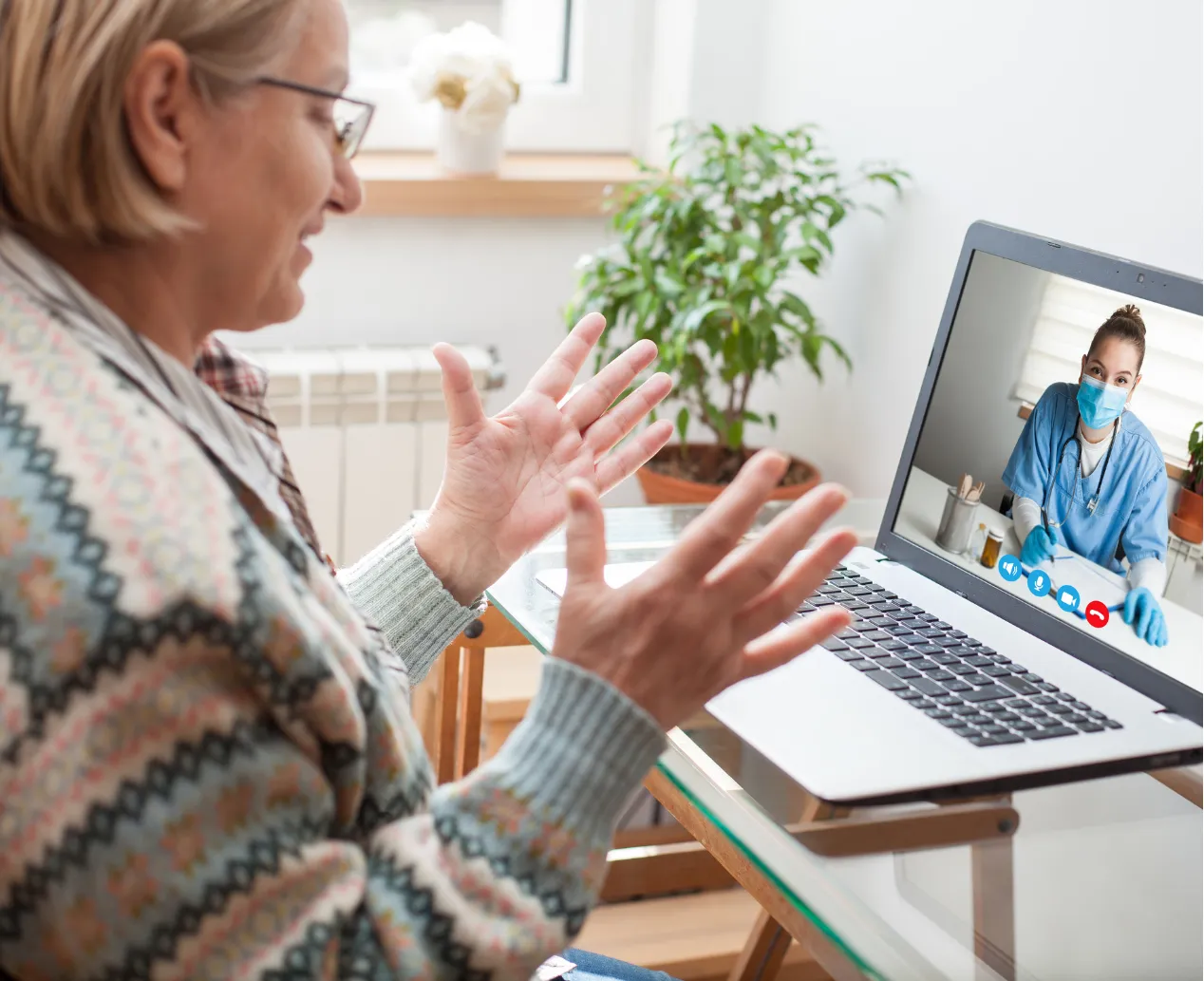 Older woman talks to a doctor in scrubs and a mask via video call on her laptop at home.